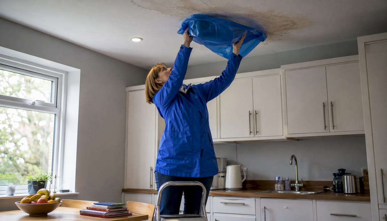 Woman covering ceiling leak with plastic sheet